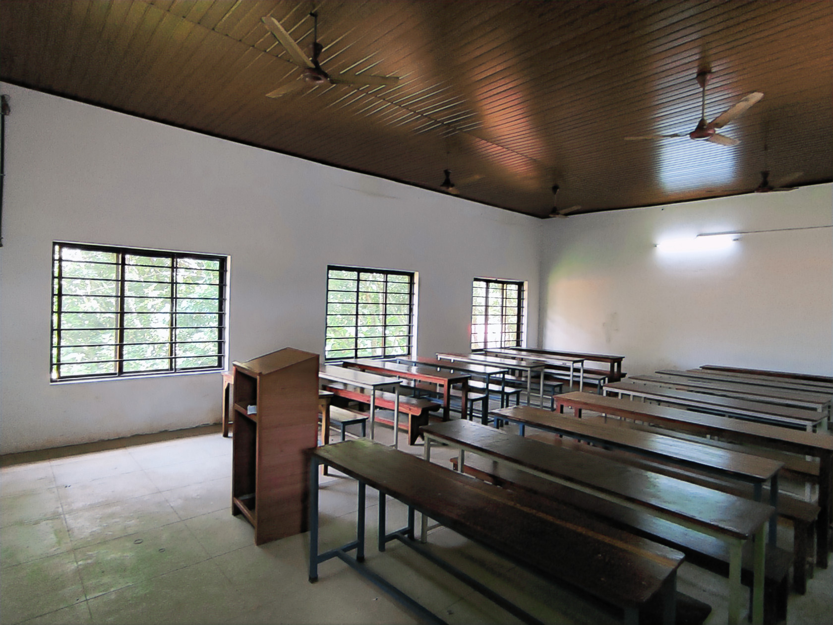 one of the lecture rooms of the college, with a lectern, student seating and three fairly large windows