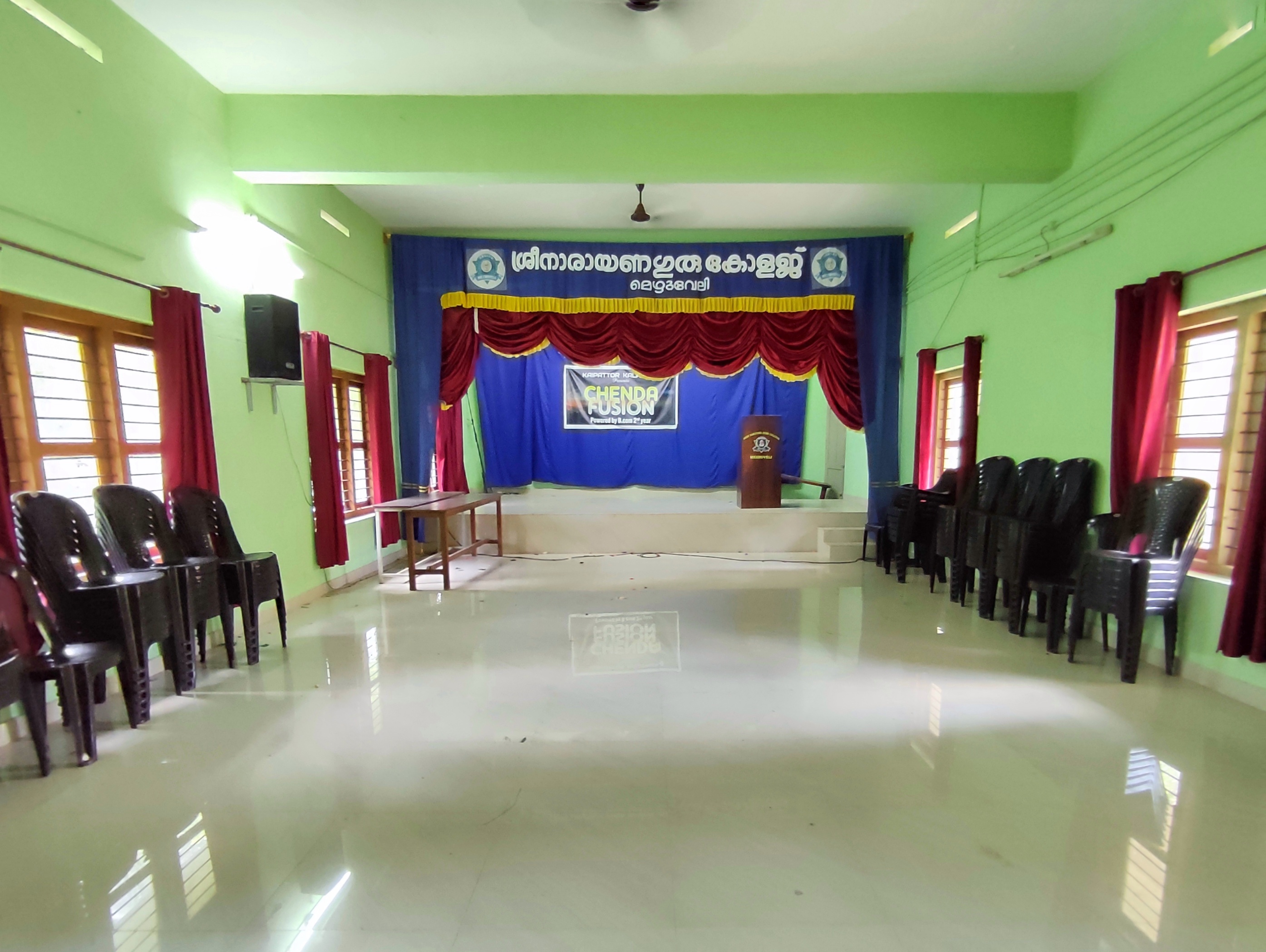 auditorium with a stage and white glossy tile flooring, chairs neatly chairs neatly arranged along the wall